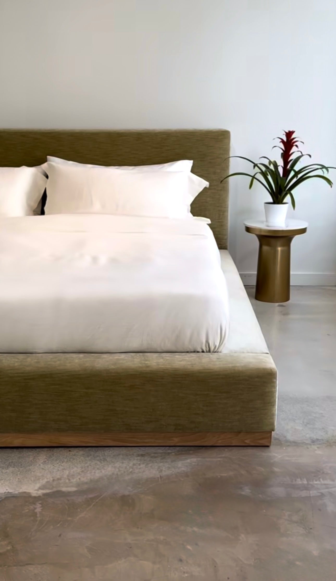 Handcrafted custom upholstered platform bed with a moss green fabric frame and white bedding in a modern minimalist bedroom.